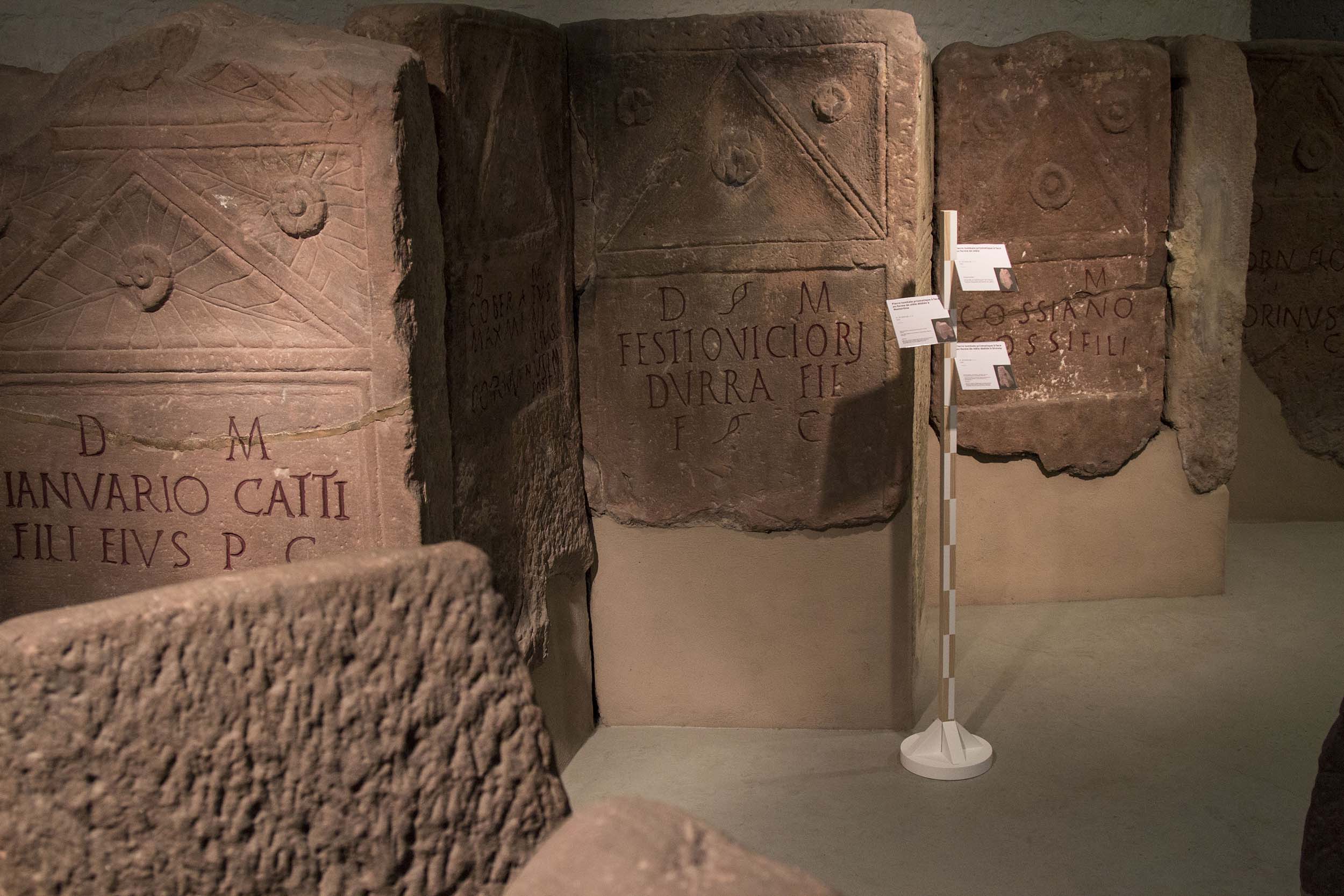 Porte-cartels sur pied en bois installé parmi les stèles de la section archéologique du Musée du Château des Rohan de Saverne
