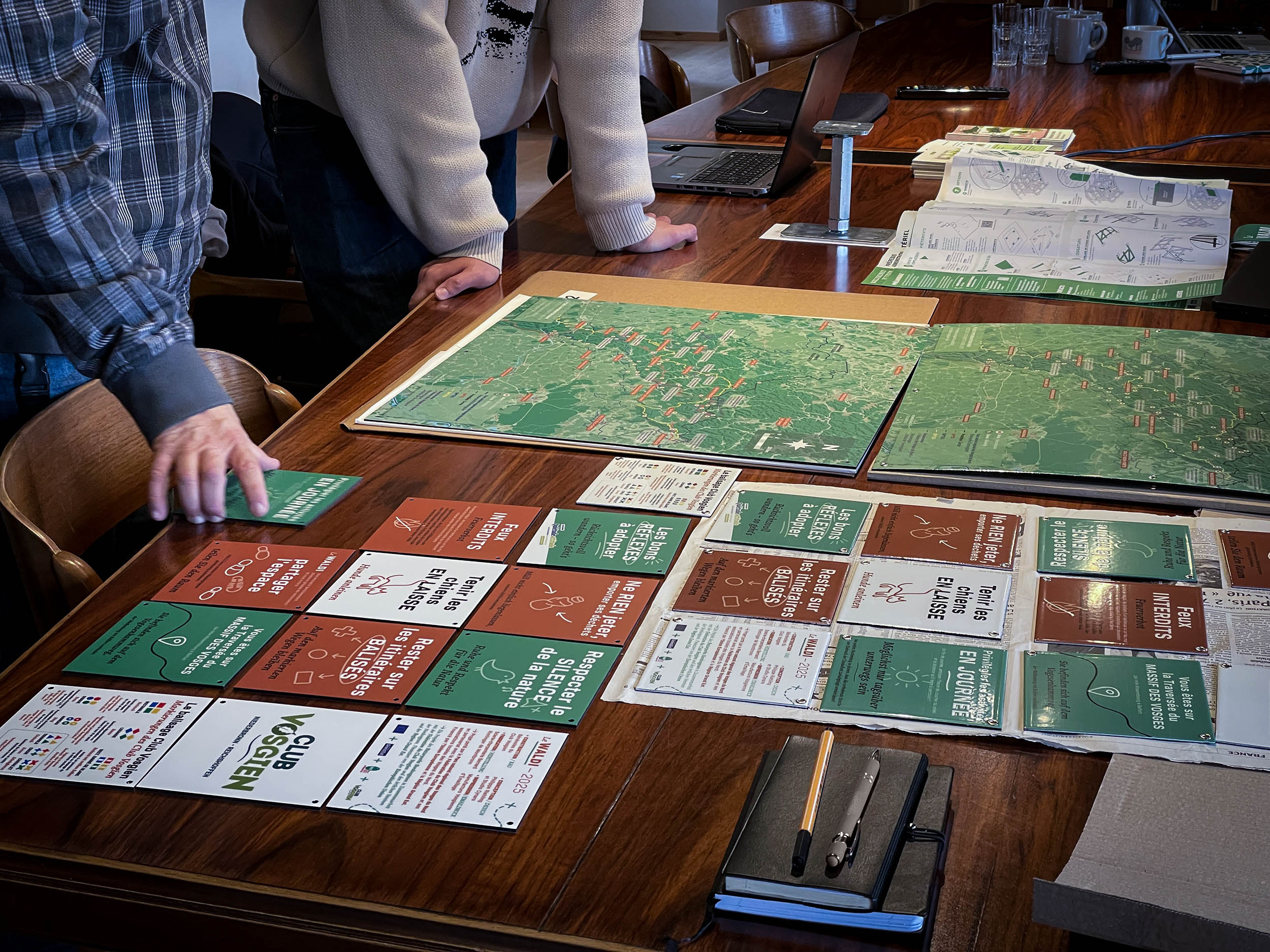 Réunion de présentation des imprimés signalétiques que l'on voit répartis sur une table en bois, les interlocuteurs autour.