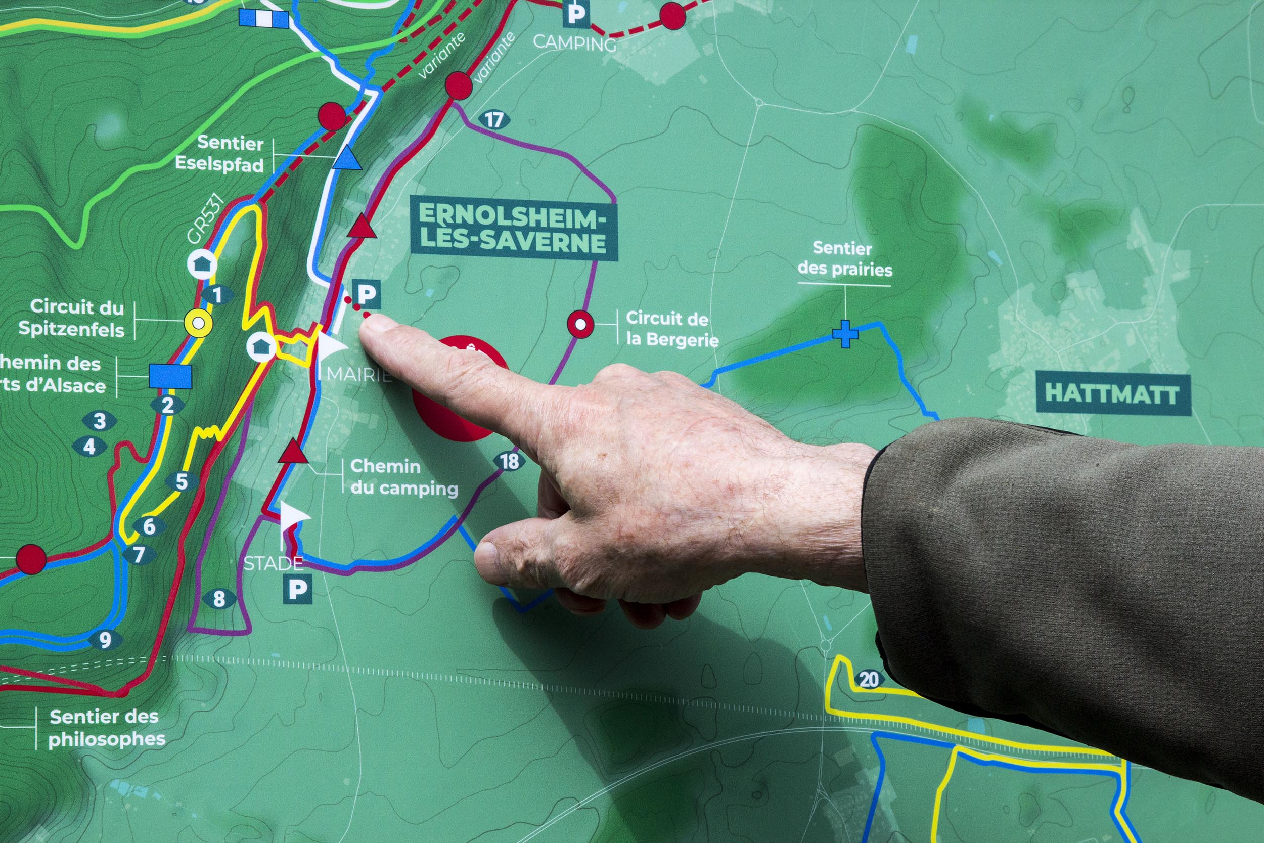 Un randonneur pointe son doigt sur un lieu du parcours, sur la carte géographique des circuits de randonnée