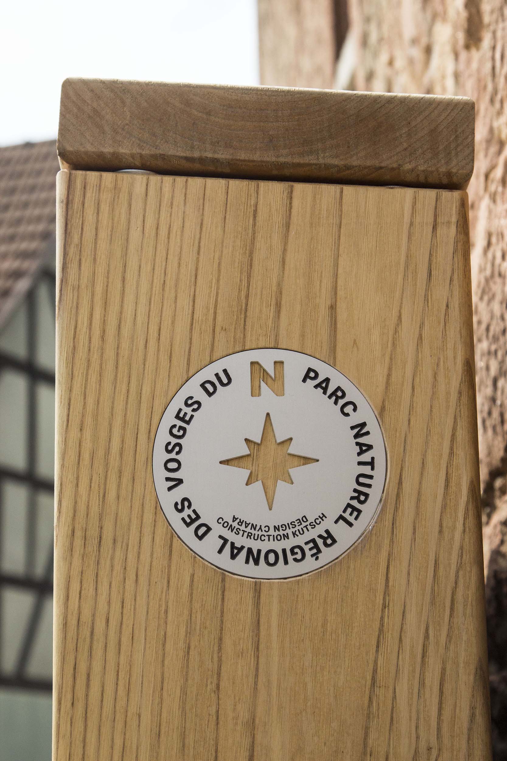 Médaillon-boussole gravé sur aluminium, en inclusion dans le mobilier, avec écrit "Parc naturel régional des Vosges du Nord, Design Cynara, Construction Kutsch"
