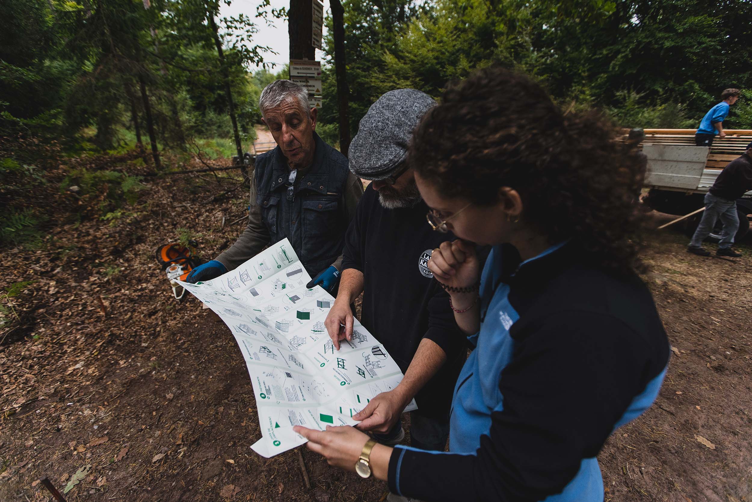 Trois personnes tiennent le grand plan papier de construction de l’abri, et réfléchissent avant de démarrer le chantier.