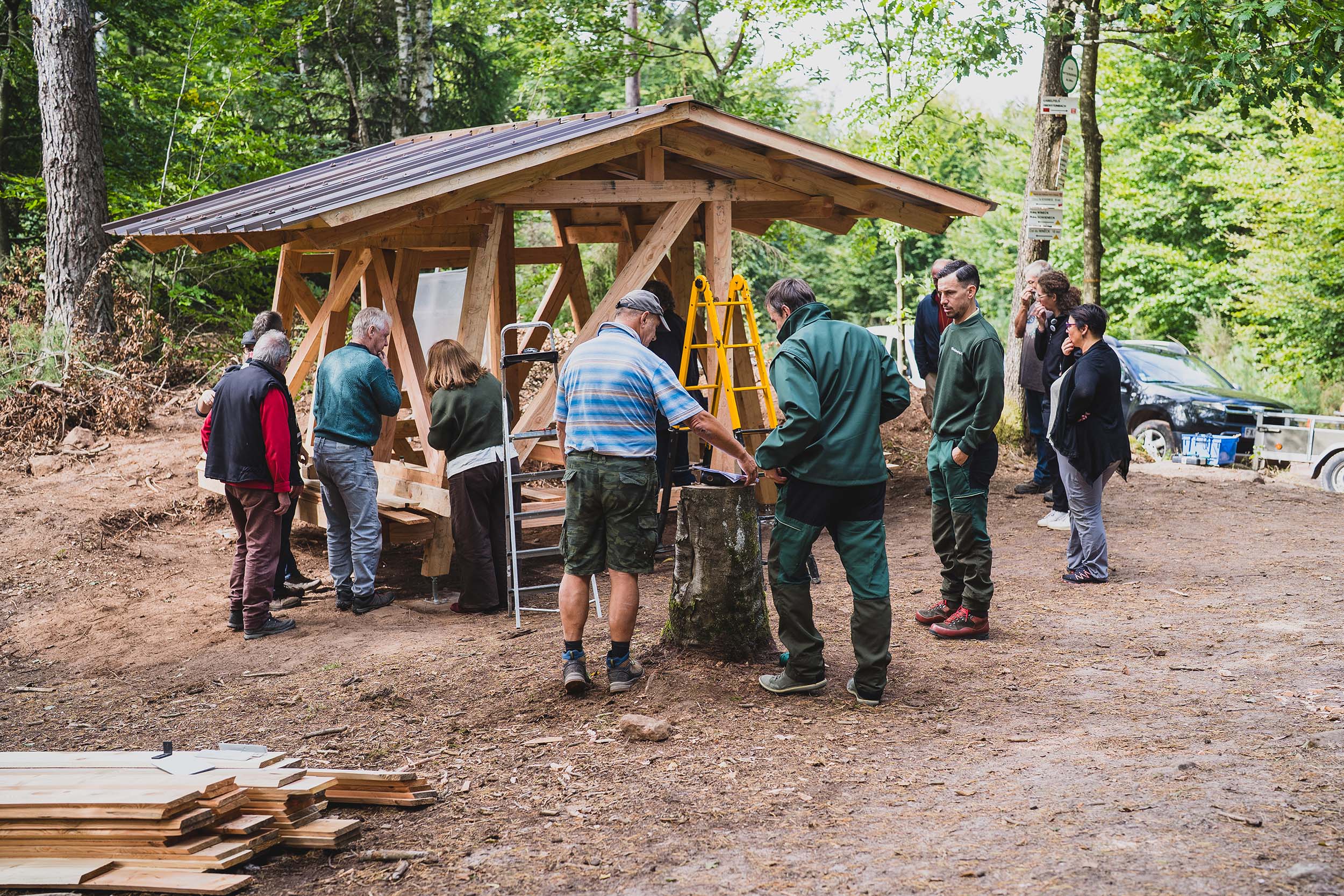 Un groupe d’une dizaine de personnes du Club Vosgien et du Parc naturel observe l’abri en cours de construction. La structure et la toiture sont là, le bardage est en cours.