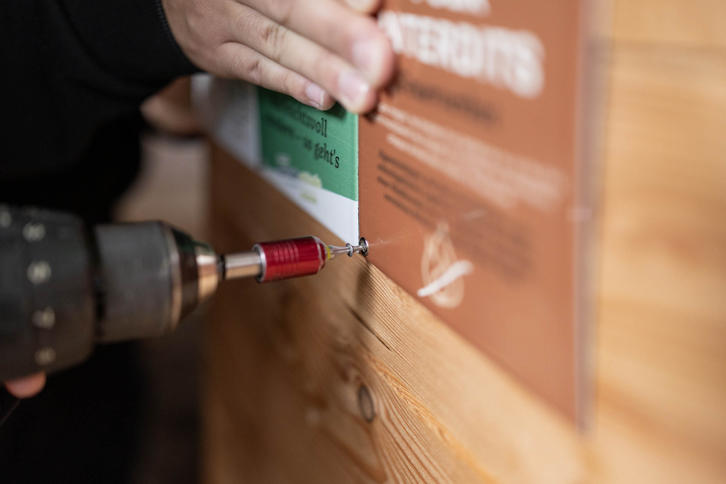 Une main appuie sur les plaques de métal émaillé pour les maintenir tandis qu'une autre main visse avec une visseuse.
